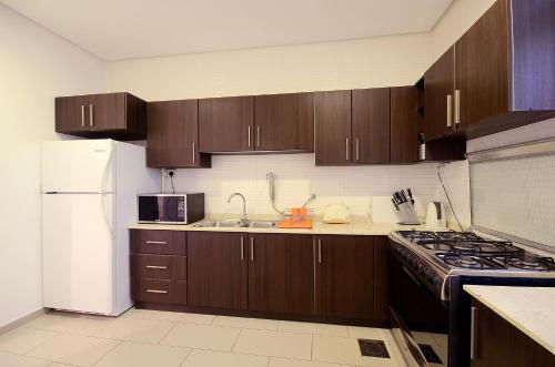 cocina con armarios de madera y nevera blanca en Code Housing - Salmiya-Family only, en Kuwait