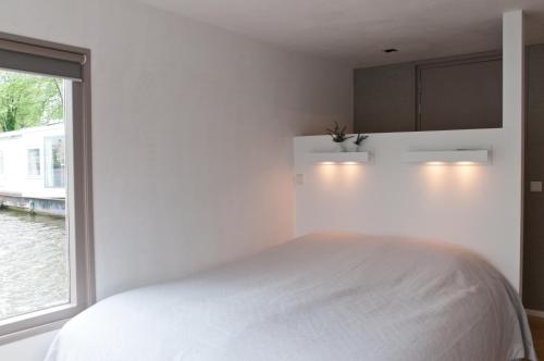 a white bedroom with a bed and a window at Houseboat Little Amstel in Amsterdam