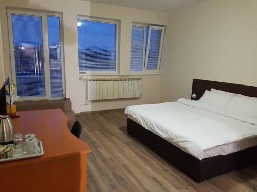 a bedroom with a bed and a desk and windows at Rooftop Oscar Rooms in Sofia