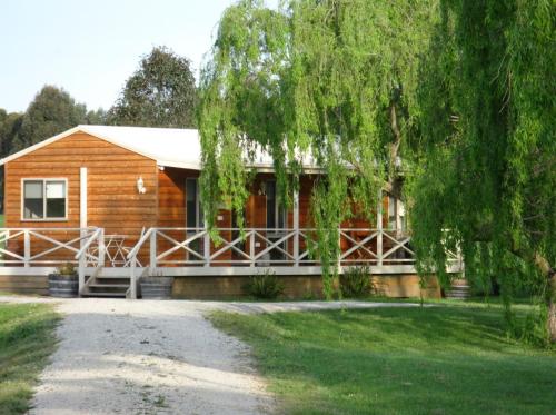 uma cabana de madeira com um alpendre e uma árvore em Little Lake Cottage em Nyora