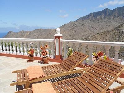 balkon z 2 drewnianymi krzesłami i widokiem na góry w obiekcie Casas Rurales El Serrillal w mieście Hermigua