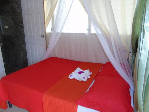 a red bed with a red blanket and a window at Hostal Villas Mexico in San Juan del Sur