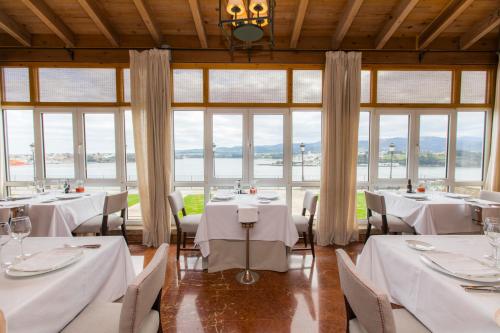 a restaurant with white tables and chairs and windows at Parador de Ribadeo in Ribadeo