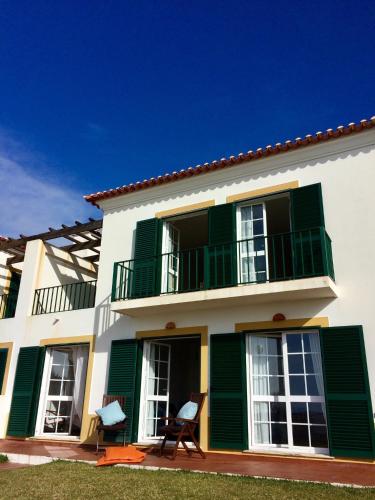 a white house with green shutters and two chairs at Casa Sol e Mar em Porto Covo in Porto Covo