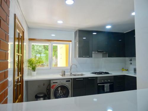 a kitchen with black cabinets and a washing machine at Condomínio jardim das oliveiras in Alcabideche