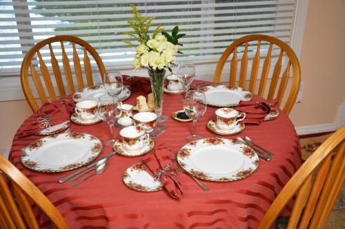 una mesa con platos y vasos y un jarrón de flores en Tea Cozy Bed & Breakfast en Qualicum Beach