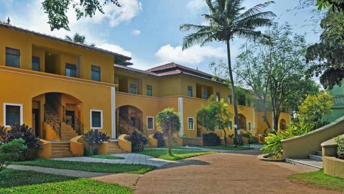 a large yellow building with a palm tree at Mercure Goa Devaaya Resort in Old Goa