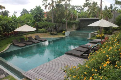 a swimming pool with lounge chairs and umbrellas at Betutu Bali Villas in Ubud