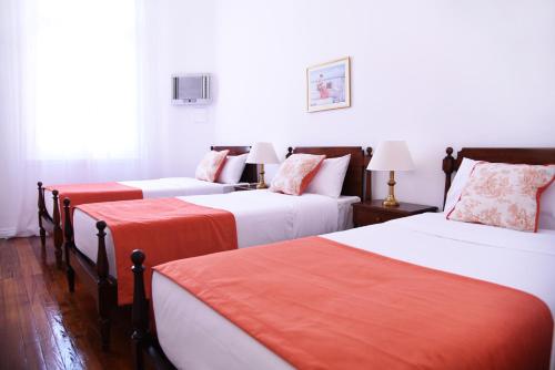 a bedroom with three beds with orange and white sheets at Gran Texier Hotel Casino in Concepción del Uruguay