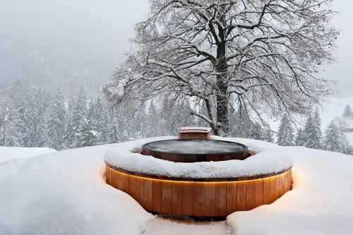 a snow covered fountain with a bench in front of a tree at La Vallée Hôtel &Spa in Lourtier