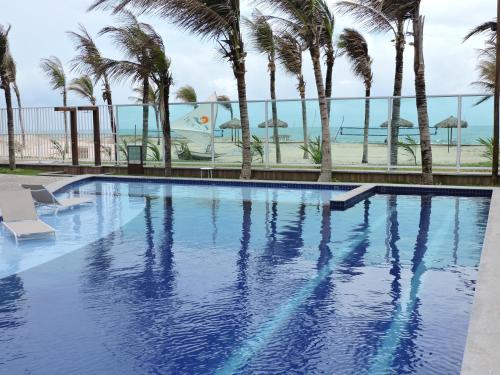 una piscina con palmeras y el océano en Apartamento com vista pro mar - Beach Way, en Aquiraz
