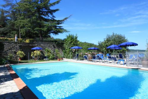 a swimming pool with blue umbrellas and people sitting in chairs at Villa Sant’Uberto Country Inn in Radda in Chianti