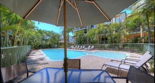 ゴールドコーストにあるBila Vista Kirra Beachside Apartmentsのスイミングプールの横にあるテーブル(傘付)