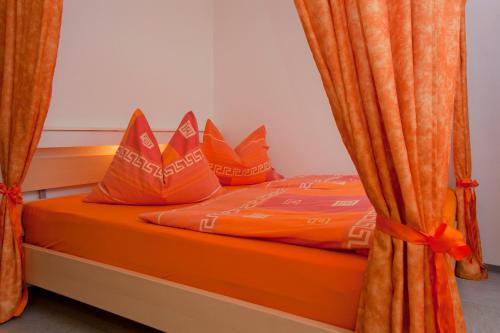a bed with orange sheets and pillows with orange curtains at Ferienwohnung Pali in Sankt Johann in Tirol