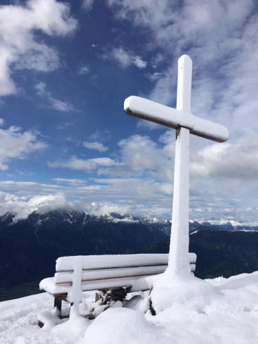 a snow covered bench and a cross on top of a mountain at Appartement Schusternagele in Amlach