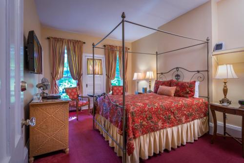 um quarto com uma cama de dossel e uma colcha vermelha em The Inn at Cooperstown em Cooperstown