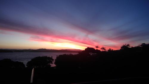 a sunset over a body of water with trees at Mason lane Apartment in Whangarei