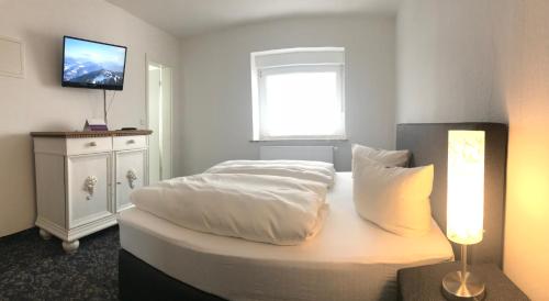 a bedroom with a bed with white sheets and a television at Alpina Lodge Hotel Oberwiesenthal in Kurort Oberwiesenthal