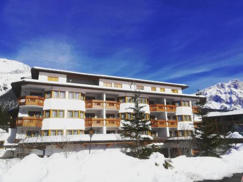 a building in the snow with mountains in the background at Aktiv-Hotel Traube am Mieminger Sonnenplateau in Wildermieming