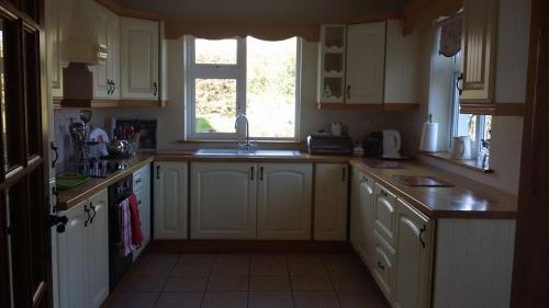 uma cozinha com armários brancos, um lavatório e uma janela em Hazel Cottage em Limerick