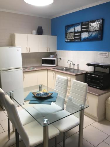 a kitchen with a glass table and white chairs at Beachlander Self-Contained Holiday Apartments in Coffs Harbour