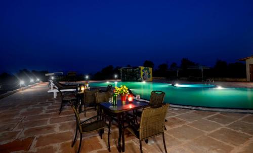 a patio with tables and chairs next to a pool at night at Tathastu Kanha in Kānha