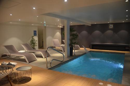 a pool in a room with chairs and a table at Hotel et Spa Les Cleunes Oléron in Saint-Trojan-les-Bains