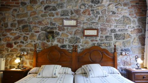 a bedroom with a wooden bed in a stone wall at Hotel Rural Los Texos in La Riera