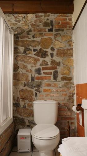 a bathroom with a white toilet in front of a stone wall at Hotel Rural Los Texos in La Riera