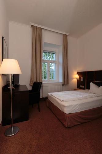 a bedroom with a bed and a desk and a window at Hotel Landhaus Schlachtensee in Berlin