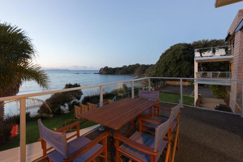 a balcony with a wooden table and chairs and the ocean at By the Bay Beachfront Apartments in Mangonui