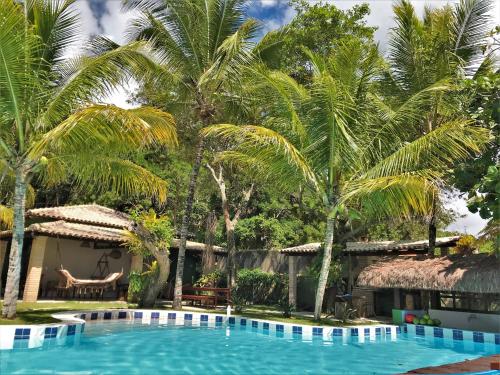 uma piscina em frente a um resort com palmeiras em Pousada Mayon em Cumuruxatiba