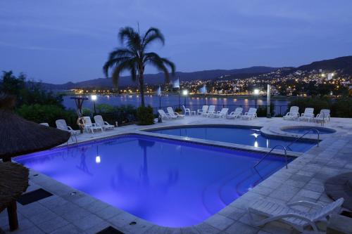 a pool with chairs and a palm tree at night at Hotel Marqués del Lago in Villa Carlos Paz