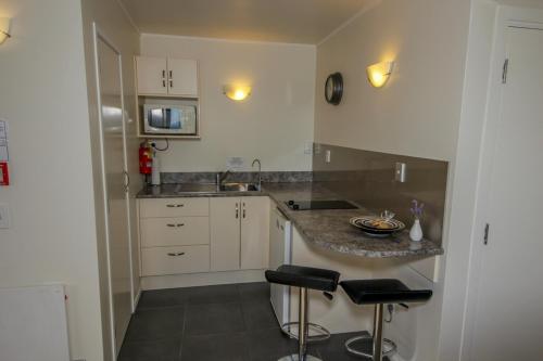 una cocina con armarios blancos y una barra con taburetes en By the Bay Beachfront Apartments, en Mangonui