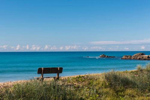 a bench sitting on the beach near the ocean at Smugglers On The Beach in Coffs Harbour