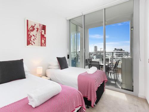 1 Schlafzimmer mit 2 Betten und einem Balkon mit Aussicht in der Unterkunft As the Sun Sets - Modern and Spacious 2BR Zetland Apartment Facing the Setting Sun in Sydney