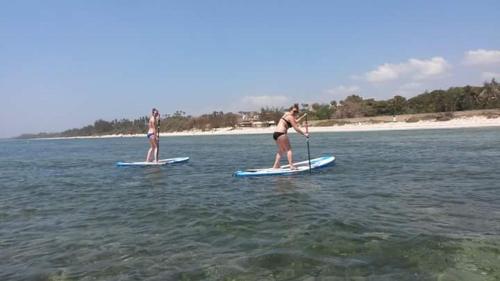 two women in bathing suits on paddle boards in the water at Mango Lodge MSAMBWENI in Kisimachande