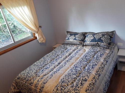 a bedroom with a bed with blue and white comforter and a window at Cabañas Kumelka in Villarrica