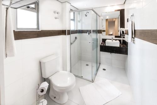 a white bathroom with a toilet and a shower at Summit Hotel Monaco in Guarulhos