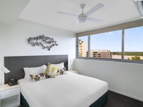 a bedroom with a white bed and a large window at Oaks Mackay Rivermarque Hotel in Mackay