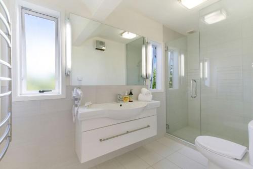 a white bathroom with a sink and a shower at The Apartment at Palm Beach by Waiheke Unlimited in Palm Beach
