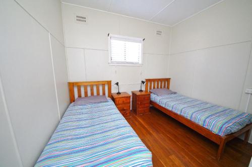 two beds in a room with white walls and wooden floors at Apollo 1, 9 Hodgson Street in Crescent Head