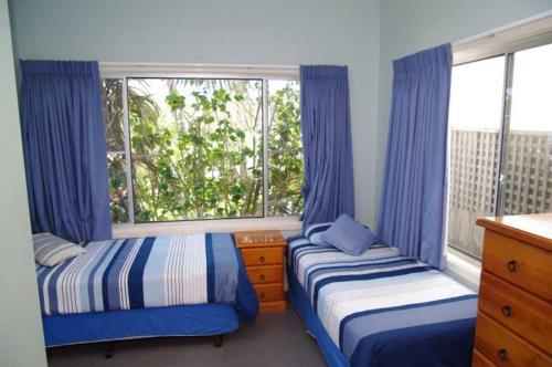 a bedroom with two beds and a window with blue curtains at Clareview, 8 Korogora Street in Crescent Head