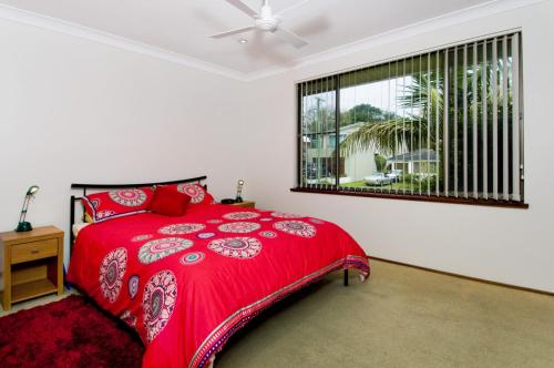 a bedroom with a red bed and a window at Cara Nobbys Beach 11 Wesley Avenue in Port Macquarie