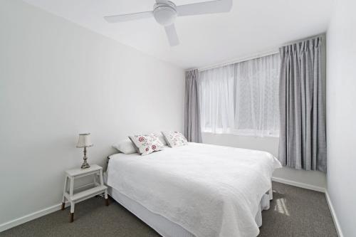 een witte slaapkamer met een wit bed en een raam bij Flynns Beach Apartments 4 41 Pacific Drive in Port Macquarie