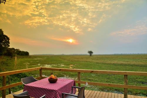 a table and chairs on a deck with a view of a field at Muchenje Self Catering Cottages in Muchenje