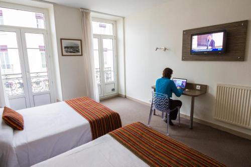 a woman sitting at a desk in a hotel room at Hôtel de l'Europe Grenoble hyper-centre in Grenoble