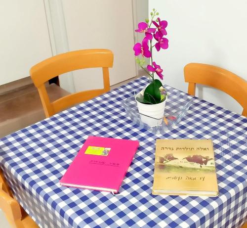 a table with two books and a vase with flowers on it at Like Home Gedera in Gedera