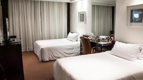 a hotel room with two beds and a desk at Plaza São Rafael Hotel in Porto Alegre