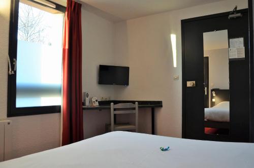 a hotel room with a bed and a desk and a television at The Originals City, Hôtel Amys, Tarbes Sud in Odos